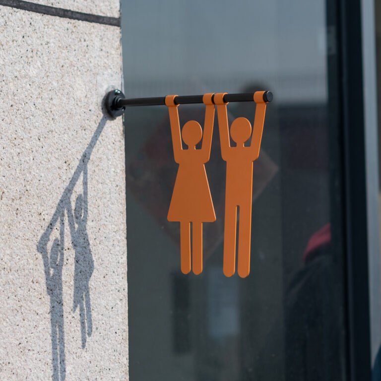 Hanging restroom sign with male and female silhouettes in a glass corridor scene
